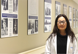 Photo of Minna Woo featuring Insulin 100 photos in the background. Taken from the hallways of the Banting and Best Diabetes Clinic at the Toronto General Hospital where the first dose of insulin was given to Leonard Thompson 100 years ago, only a year after the discovery of insulin.